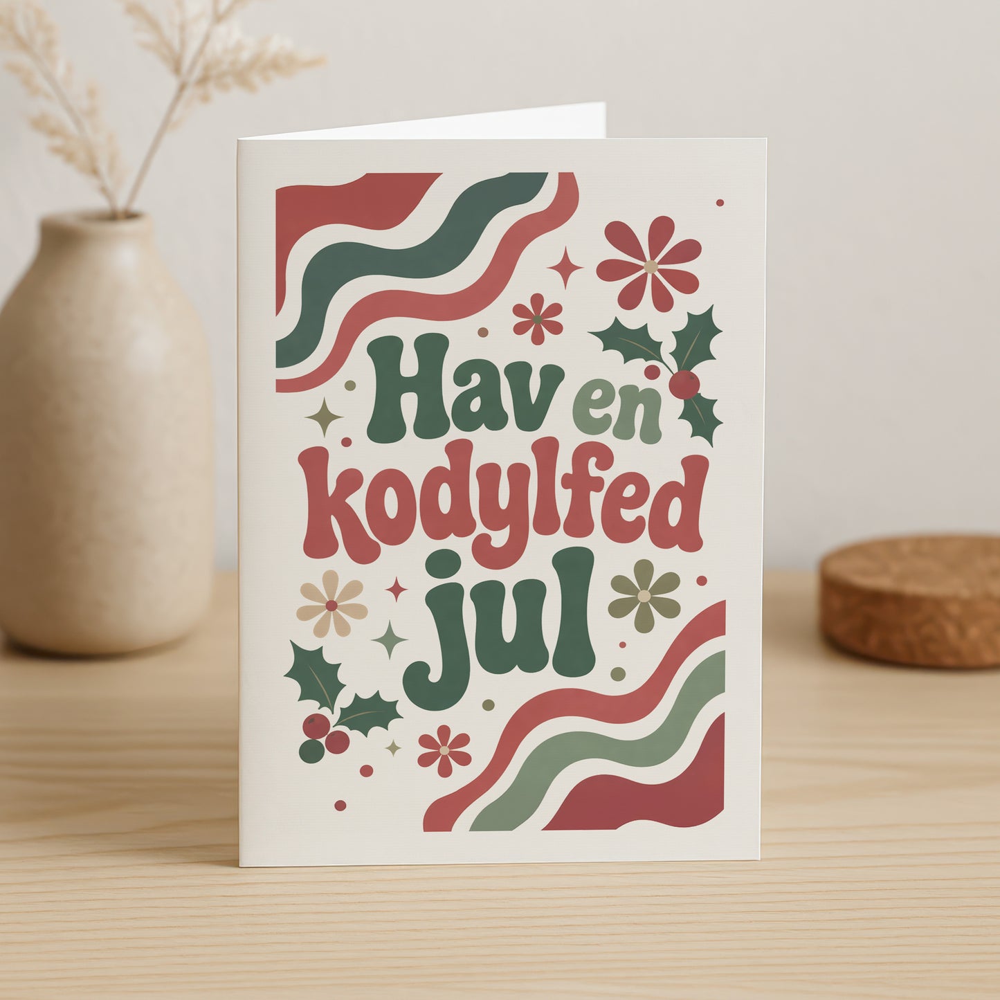Retro dobbeltkort i 70'er stil med teksten Hav en kodylfed jul omkranset af kristtjørn, bær og bølgede julemønstre.